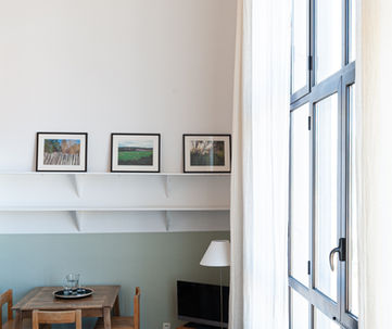 Salon lumineux, coin repas, grande fenêtre, tableaux, mobilier moderne.