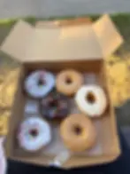 Assorted glazed and sprinkled donuts in an open box.