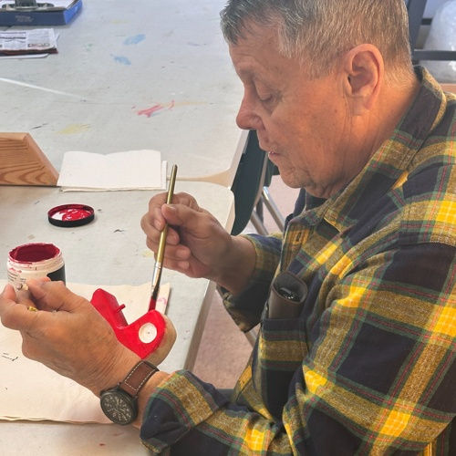 Man in a yellow flannel shirt painting a small red object