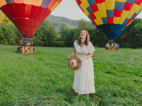 Woman laughing while holding hat. Two hot air balloons and mountains in the background