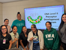 A group of people in a room smiling with a sign in the background.