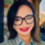 A lady with short black hair, wearing black frame glasses and red lipstick smiling.