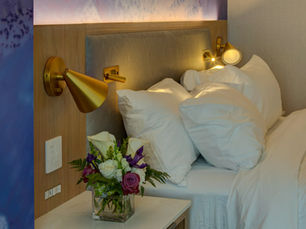 Elegant hotel bed with plush white linens, gold lighting, and fresh flowers on a marble nightstand.