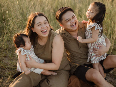 Parents laughing with toddler and baby in warm golden light – Bicentennial Park sunset – natural unposed family photos.