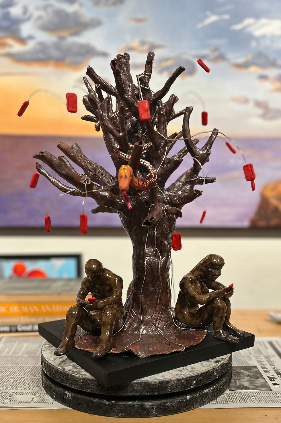 A sculpture showing a tree with smart phones and adam and eve under it, representing the forbidden fruit in digital form as apples