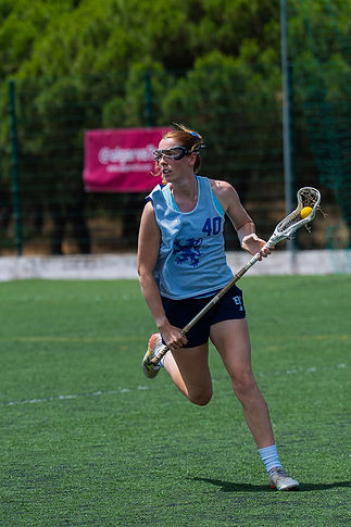 Female athlete running with a lacrosse stick on a field