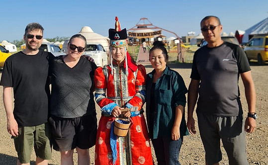 Two tourists with two Mongolian men in casual clothes and a Mongolian woman in traditional dress, standing together in the steppe