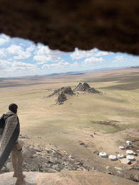 A person standing alone in a vast, arid, undeveloped landscape with distant hills in Mongolia. Solitude, vast landscapes, remote travel.