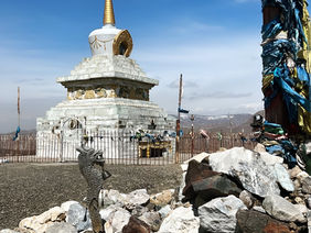 White Buddhist stupa or chorten with prayer flags in a rocky, mountainous setting under a bright sky. Mongolian temple, Buddhist architecture, spiritual landmark.