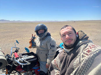 Two people warmly dressed, standing next to a motorcycle in a rugged, open landscape in Mongolia. Winter motorcycle tour, adventure partners.