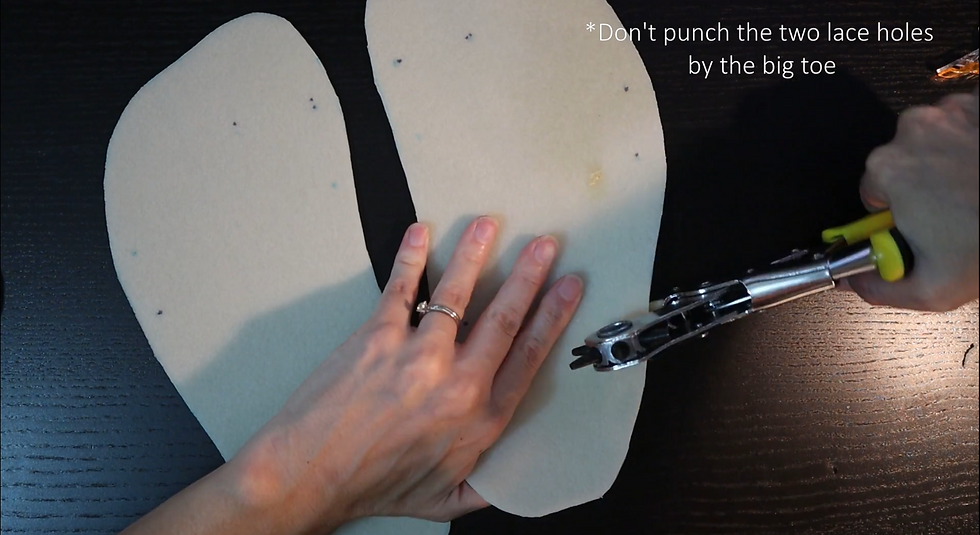 Hands holding a leather hole punch above two light beige shoe soles on a dark surface. Text: "Don't punch the two lace holes by the big toe."