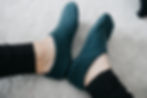 Feet in teal slippers, seen from above on a light gray carpet. Person wears black leggings. Cozy and relaxed atmosphere.
