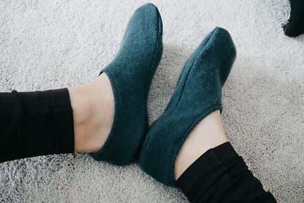 Feet in teal slippers, seen from above on a light gray carpet. Person wears black leggings. Cozy and relaxed atmosphere.