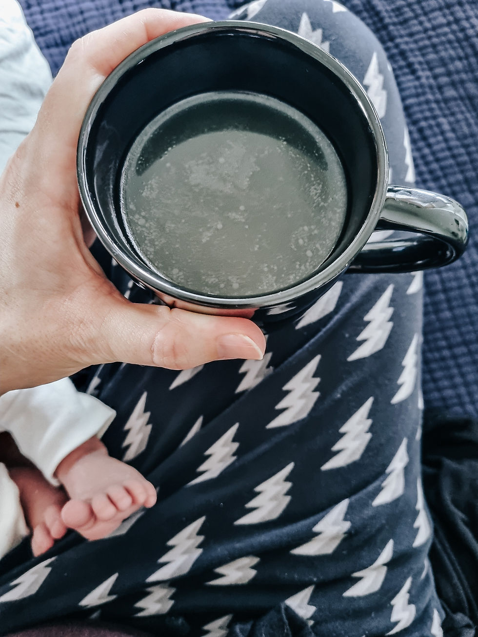 Person holding a black mug over lap, wearing navy pants with white zigzag pattern. A baby's foot is visible, creating a cozy mood.