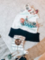 Baby in a star-patterned onesie on a blanket with a wooden toy and yarn nearby. A bowl of food sits on a checkered towel. Cozy ambiance.