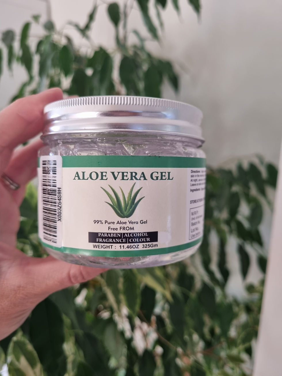 Hand holds jar of Aloe Vera Gel with green label, plant in background. Text: 99% Pure Aloe Vera Gel, Free from Paraben, Alcohol.