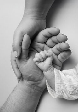 Manos de padres sosteniendo la pequeña mano de recién nacido en blanco y negro.