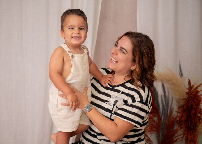 Madre sonriente abraza a su bebé feliz en sesión de maternidad.