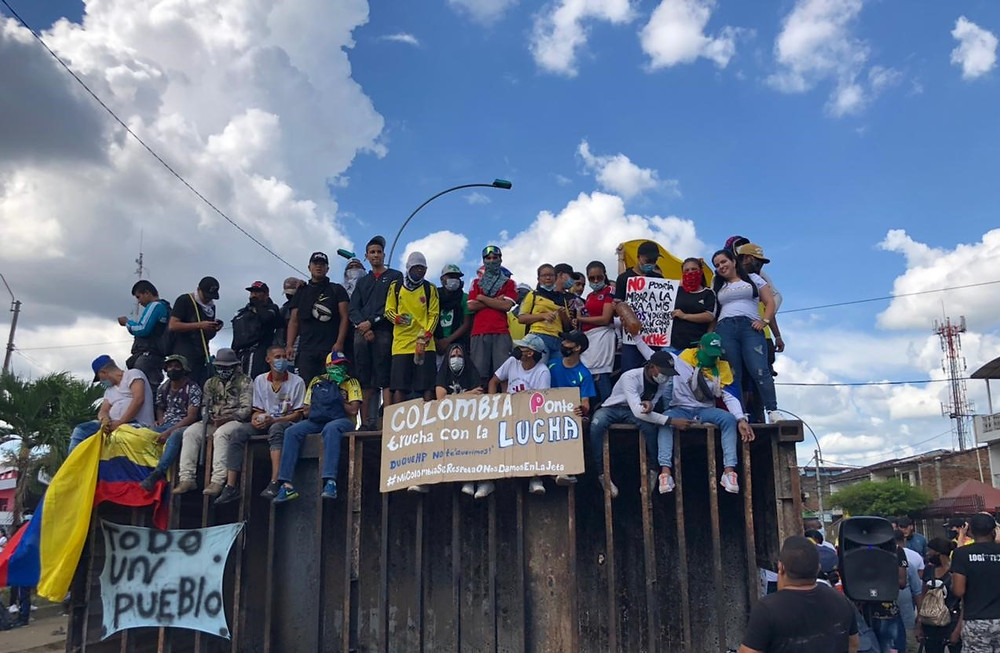 People gather to protest tax reform and government corruption in Cali, Colombia, carrying signs and flying the Colombian flag.