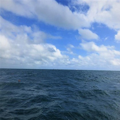 Imagem com vista para o Oceano Atlântico na parte inferior com pequenas ondas e na parte superior o céu azul com nuvens brancas