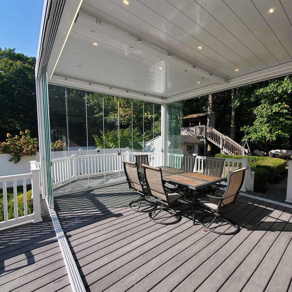 Privlux pergola converted into a patio with glass walls, wooden table, and chairs. Surrounded by trees and greenery, under a blue sky with soft lighting.