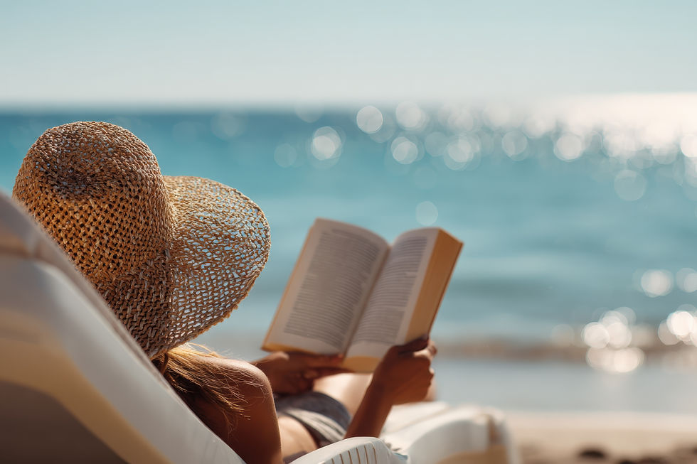 Woman relaxing on beach reading a book with blue ocean backdrop.