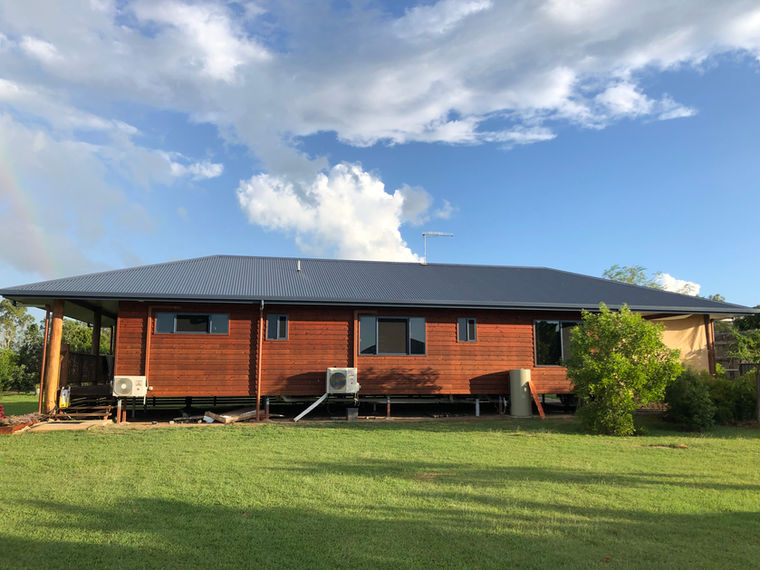 A new house with western red cedar weather boards on green lawns and blue sky behind it