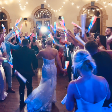 Bride and groom dancing surrounded by guests holding glowing light sticks.