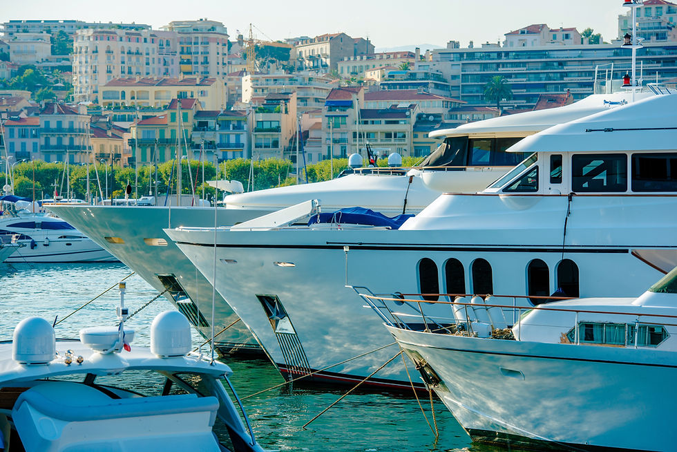 Luxury yachts docked in a marina against a backdrop of colorful seaside buildings under a clear blue sky. Calm, serene atmosphere.