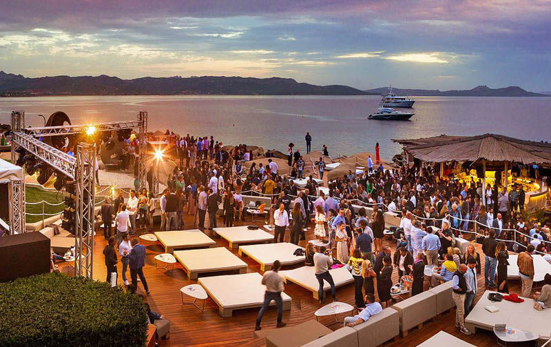 Sunset beach club party in Costa Smeralda with people enjoying music and cocktails.