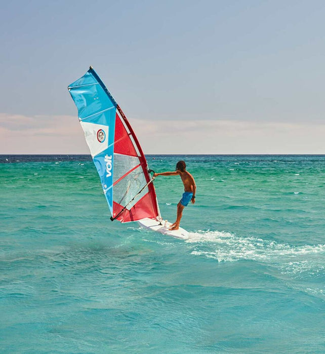 Windsurfer gliding across turquoise waters on the coast of Sardinia.