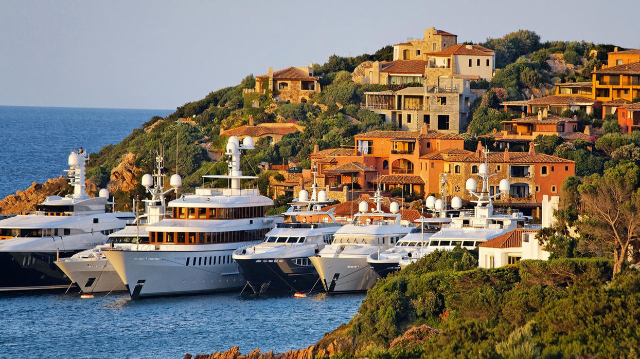 Luxury yachts docked in Porto Rotondo surrounded by hillside villas, Sardinia, Italy.