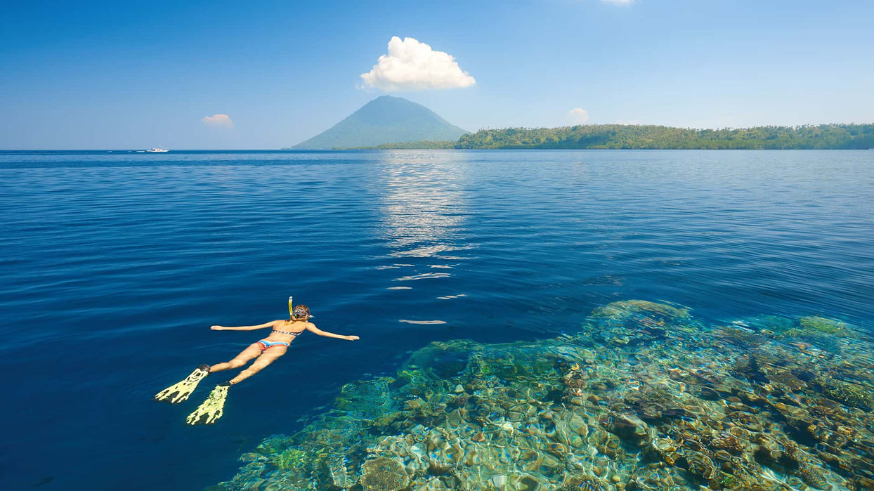 Traveler snorkeling above coral reef with volcanic mountain backdrop in Sulawesi, Indonesia
