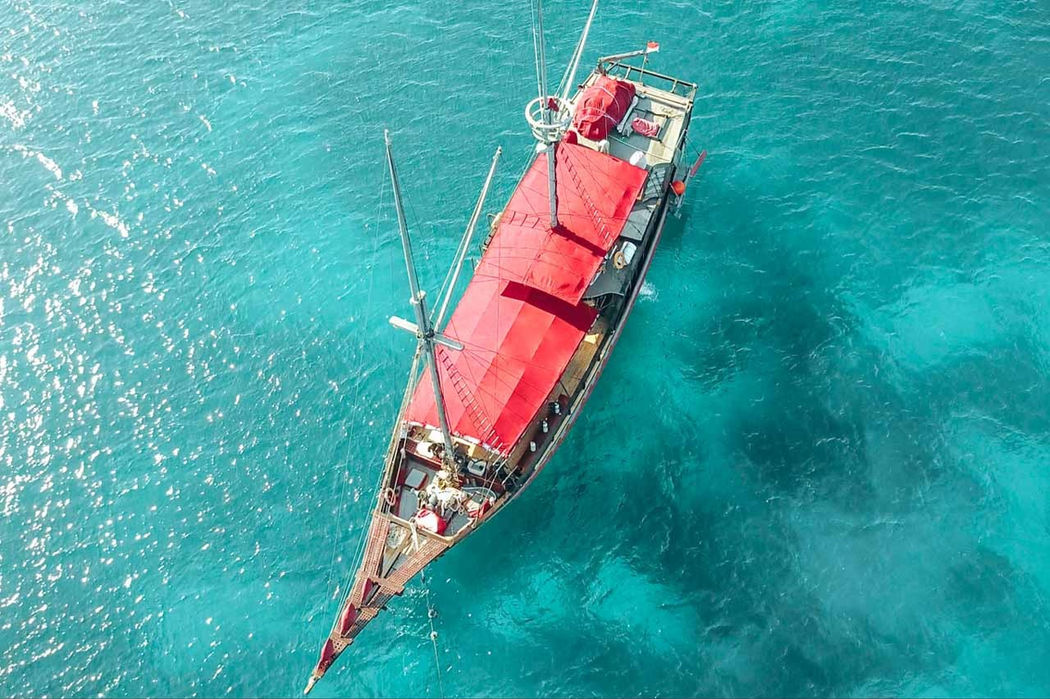 Aerial view of Mantamae phinisi yacht with red sails cruising in turquoise waters