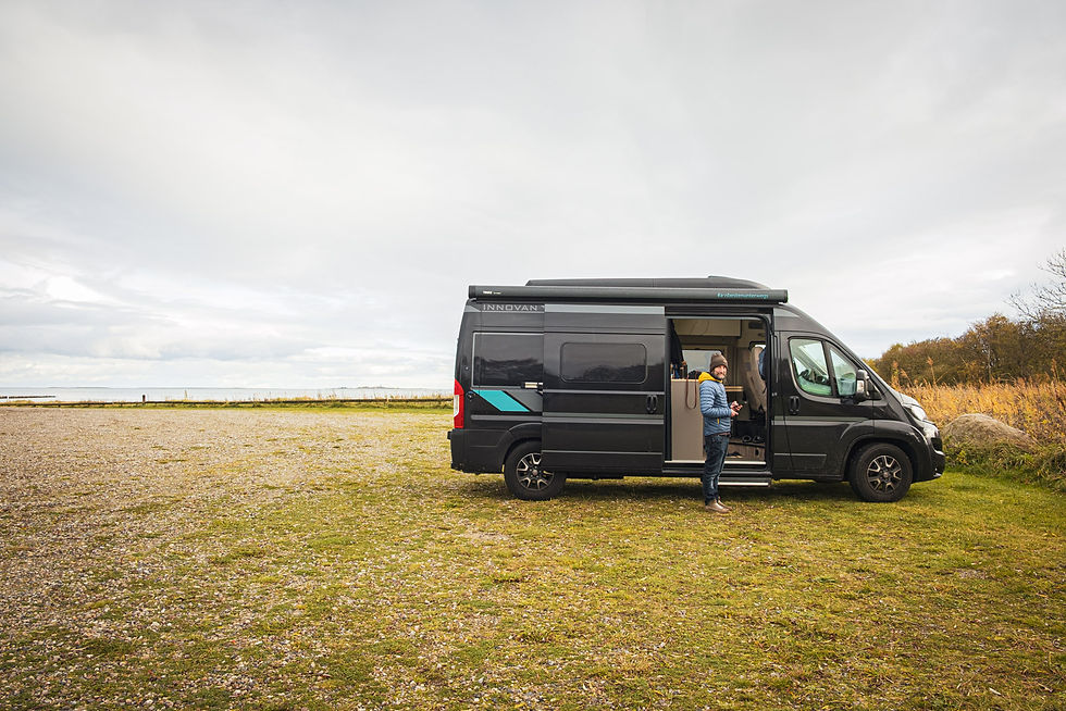 Mann vor schwarzem Campervan am Seeufer unter grauem Himmel, Tür offen; Aufschrift INNOVAN.
