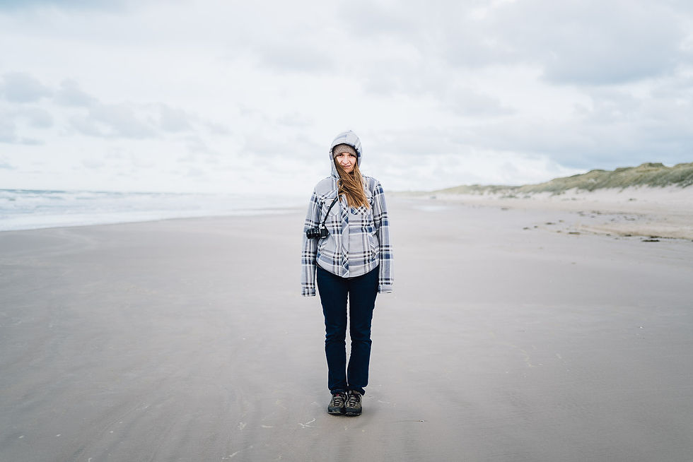 Person in kariertem Kapuzenpullover steht an einer windigen Küste und blickt aufs Meer.