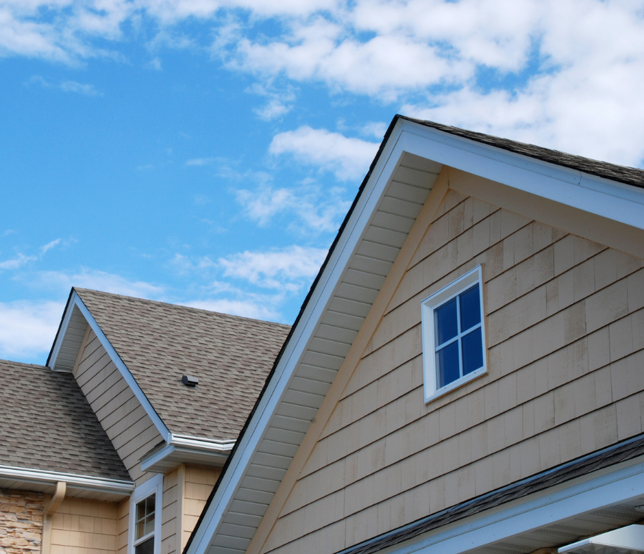 Roof of a beige house with a small window, set against a bright blue sky with scattered clouds, creating a peaceful mood.