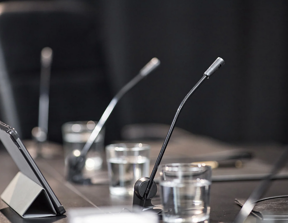 Conference table with slim gooseneck microphones and water glasses, set for a quiet meeting or press briefing.