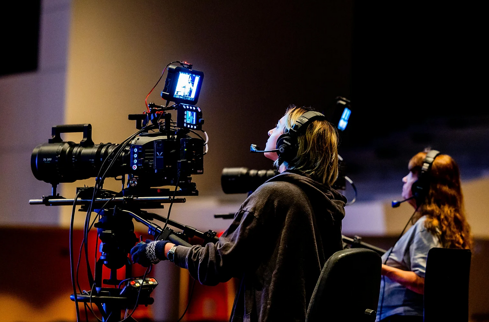 Camera operators in headsets manage large cameras indoors, focused and intent. Dark, dimly lit background.