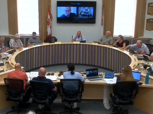 People seated around a circular table in a conference room with a screen displaying a video call. Canadian flag in the background.
