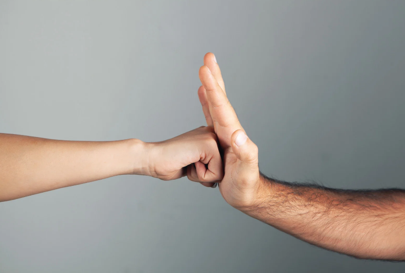 Two hands meet in a fist bump against a plain gray background, one palm upright and one fist extended.