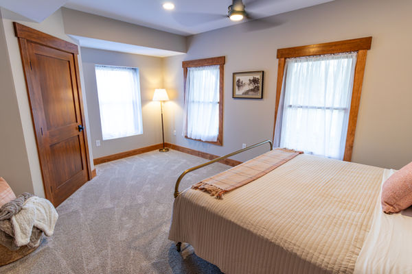 Basement bedroom with a bed, ceiling fan and several windows.