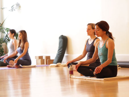 People sitting calmly on meditation cushions in a bright yoga studio