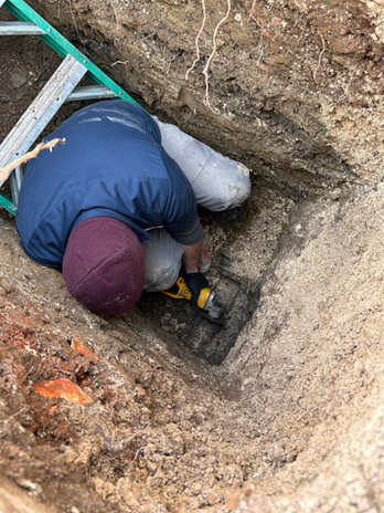 Plumber repairing an underground sewer or water line in a trench