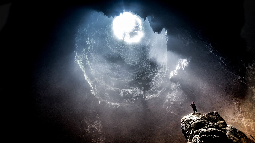 man in cave staring at light above