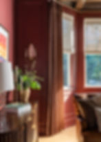 Moody parlor featuring custom Euro pleat drapery, Roman woven shades, and rich clay-colored walls in Benjamin Moore Beaujolais. A cozy, sophisticated interior with layered window treatments, warm textures, and tailored finishes by Asha Maia Design. Asha Maia Design creates timeless interiors in Arlington, Virginia, Alexandria, Virginia, and Birmingham, Michigan.
