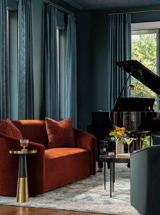 Moody salon with grand piano, rust velvet curved sofa, and deep teal walls in a modern classic interior design project in Falls Church, Virginia