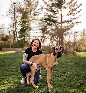 A dog trainer smiles at the camera while a great dane puppy sits on her lap