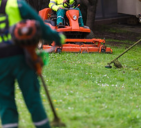 Three landscapers in uniform mowing and cleaning a green grass area with lawn equipment, f