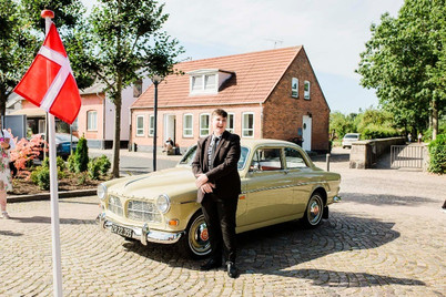 Ung konfirmand i jakkesæt foran flot gul vintage bil